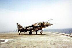 A Harrier on the deck of a small aircraft carrier, with its nose wheel off the deck