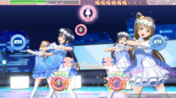 The player is playing "Yume no Tobira" with four buttons, hitting Perfects. The heads-up display features the Clear Gauge on the top-left, which is currently near the B Rank. Their score, currently has 18855 points, is on the top-right. And the stars with individual alphabet which would spell out "Love Live!", currently has "L O V E L I", is at the top. The 3D animated music video in the background, which Kotori, Nozomi, Umi, and Rin are performing in its respective costume set on the rooftop in the city.