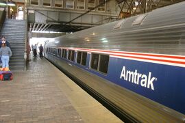 Stainless steel passenger rail cars with a thick blue stripe across the windows and two thinner red stripes above