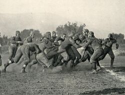 A cluster of American football players colliding on a dirt field