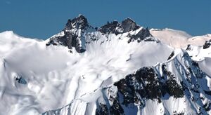 A dark rugged mountain towering over glacial ice and rock on a clear day.