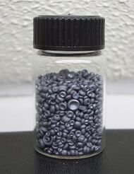 A small glass jar filled with small dull grey concave buttons. The pieces of selenium look like tiny mushrooms without their stems.