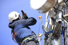 A worker using a personal RF safety monitors on a mast, near antennas.