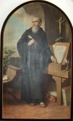 painted portrait of St.Benedict standing by a desk writing his Rule