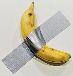 A yellow banana attached to a white wall by a piece of silver-colored duct tape