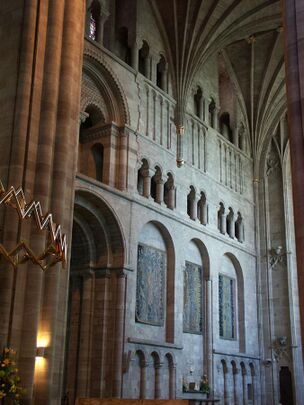 A transept interior with a wall panelled with shallow Norman arches and open galleries.