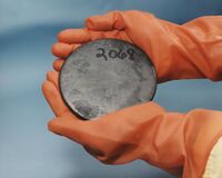 A disc of uranium being held by gloved hands