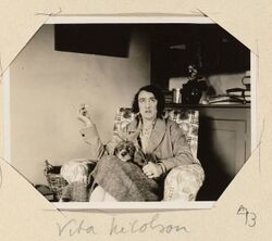Photo of Vita Sackville-West in armchair at Virginia's home at Monk's House, smoking and with dog on her lap