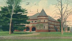 A damaged postcard showing a two-story gray building behind two trees.