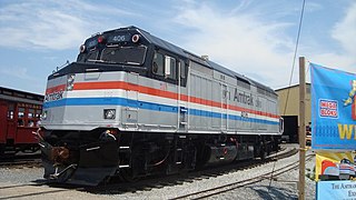 A gray diesel locomotive with a black cab area. Red, white, and blue stripes run along the sides and wrap across the front