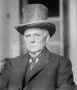 Clark dressed in a suit and tie and furry top-hat with an austere expression