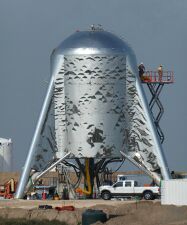Photograph of a short steel rocket stage with its fins touching the ground