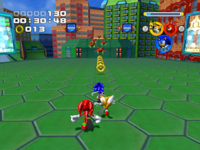 Gameplay screenshot from Sonic Heroes. In it, the cartoonish animals Sonic, Tails, and Knuckles run on top of a building in the Grand Metropolis level; there are gold rings and red hovering robots in front of them. The background depicts high-tech buildings and more of the level's geometry. The score, time, and rings collected are in the upper left corner.