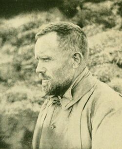 Profile photograph of a man apparently in his thirties, with short dark hair, a neatly trimmed full beard, heavy eyebrows and a high round forehead. He is dressed for outdoor work in cool weather, and is photographed outdoors squinting into the distance.