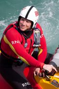 RNLI crewman seated in small inflatable, wearing helmet and bright red wetsuit.