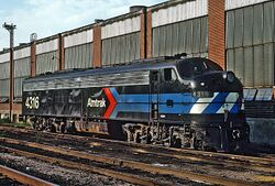 A black diesel locomotive with the Amtrak "pointless arrow" logo on the side. The blue stripes of the logo wrap around the front, where they are checked with white.