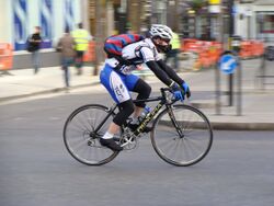 A man with sports clothes and a white helmet on a bicycle on a road.