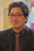 A middle-aged Japanese man with glasses, a black suit, and a red tie.