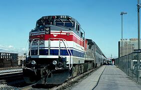 A gray diesel locomotive with red, white, and blue stripes wrapping around the sides and front. There is one wide stripe of each color, plus several narrower stripes.