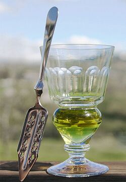 stemmed reservoir glass containing a green-colored liquid and a flat, slit, absinthe spoon