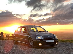 A Pearl Black Phase1 172 parked at the centre of the frame, backlit by the setting sun on the summit of a mountain pass.