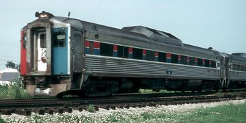 Stainless steel passenger rail cars with red and blue stripes horizontally across the windows. The visible end is covered with three vertical red, white, and blue stripes.