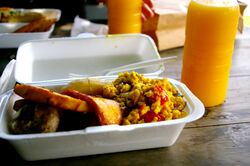 A Styrofoam container of food, plastic fork, and glass of juice