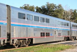 Stainless steel bilevel passenger rail cars with a blue stripe and two thinner red stripes between levels, plus a red sill stripe