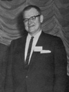 A candid photograph of a man wearing glasses and a suit