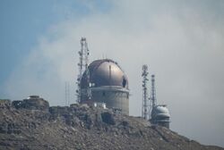 An observatory on a mountain, against a blue sky and a white cloud.