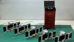 Small PicoSatellites lined up on a white table in a lab.