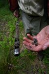 A researcher’s right hand holds out a thin metal sediment corer containing wetland soil from Morrow Mountain. The left hand holds out small bits of soil in the foreground of the image.