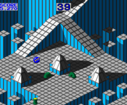 Horizontal rectangular video game screenshot of the arcade version that is a digital representation of a grided plane with ramps and spikes. A blue marble is near the center of the screen, with moving green tubes below it.