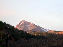The highly eroded North Sister volcano sits above a forested area, with some ice and snow visible scattered across the mountain.