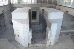 A subterranean room containing a circular structure divided into two halves. The structure is visibly weathered and has been hollowed out.