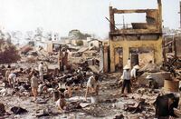 A number of Asian civilians standing amid ruined buildings and rubble.