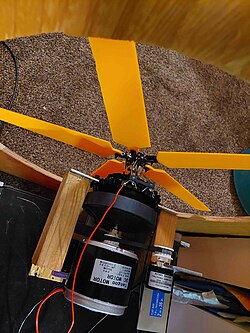 a rotary subwoofer consisting of a motor with a shaft that goes through a subwoofer which actuates a RC helicopter swashplate. The fan has 5 blades and the blades are surrounded by a plywood baffle.