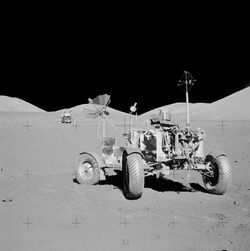 Black and white photo of a lunar rover with a lunar landing module in the background.