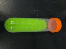 yellowish green crystals in a transparent vial with an orange ribbed screw on cap
