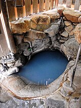 An image of a hot spring bath carved out of rock in a wooden building.