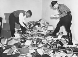 An image of two men sifting through a large pile of books on the floor at the Institut for Sexualwissenschaft.