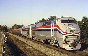 A gray diesel locomotive with red, white, and blue stripes of equal width on the side. The stripes narrow and angle downwards on the front.
