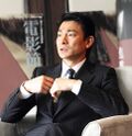 A serious-looking Andy Lau, seated and wearing a suit