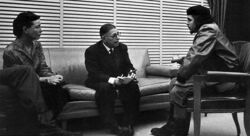 A man and a woman, both middle aged, sit and talk with a younger man, all facing away from the camera.