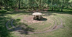 A a concrete model of a flying saucer in a clearing. There are concrete paths beneath and around the model.